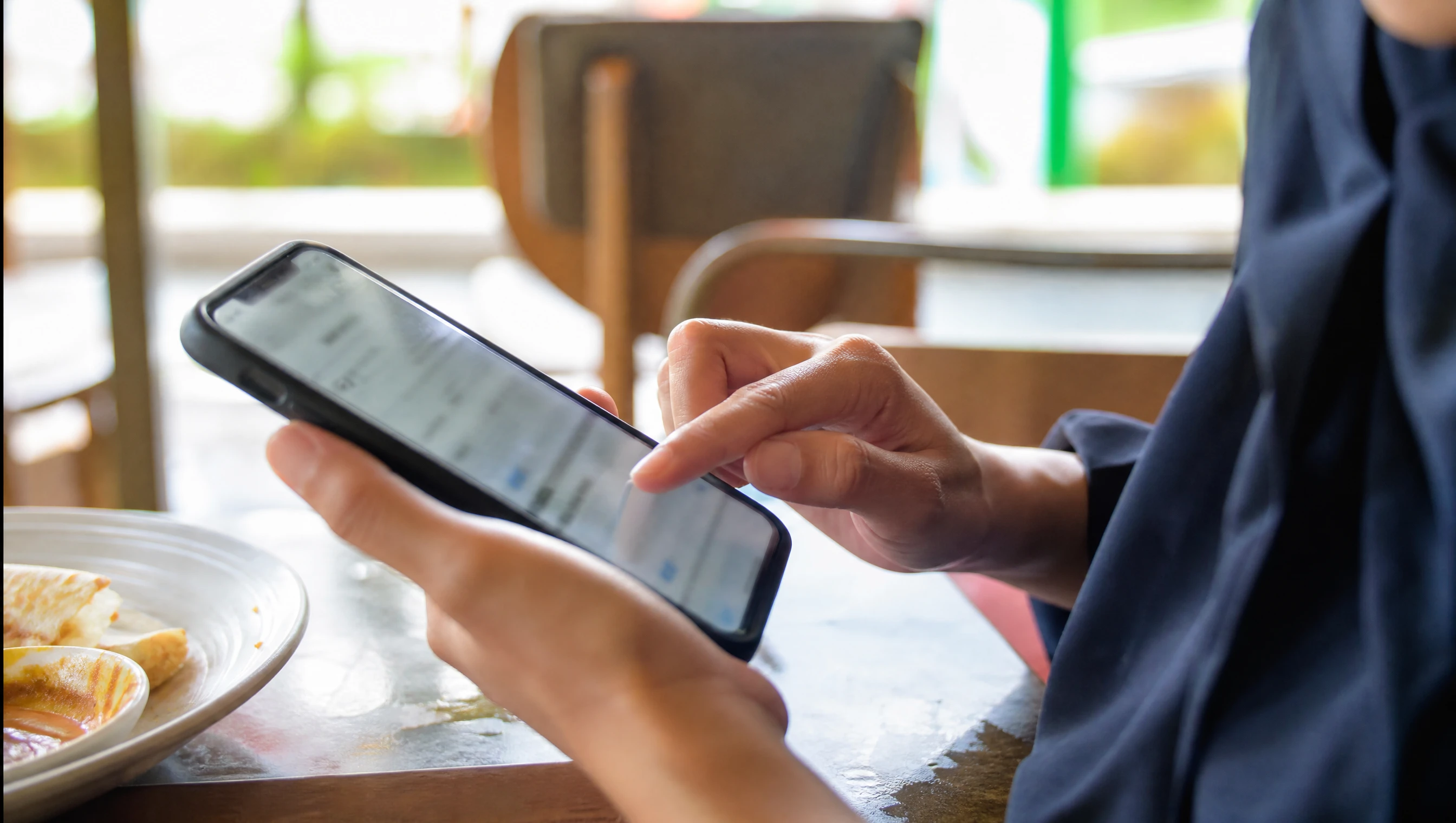 Pelanggan Malaysia menaip carian di Google pada telefon di sebuah kafe