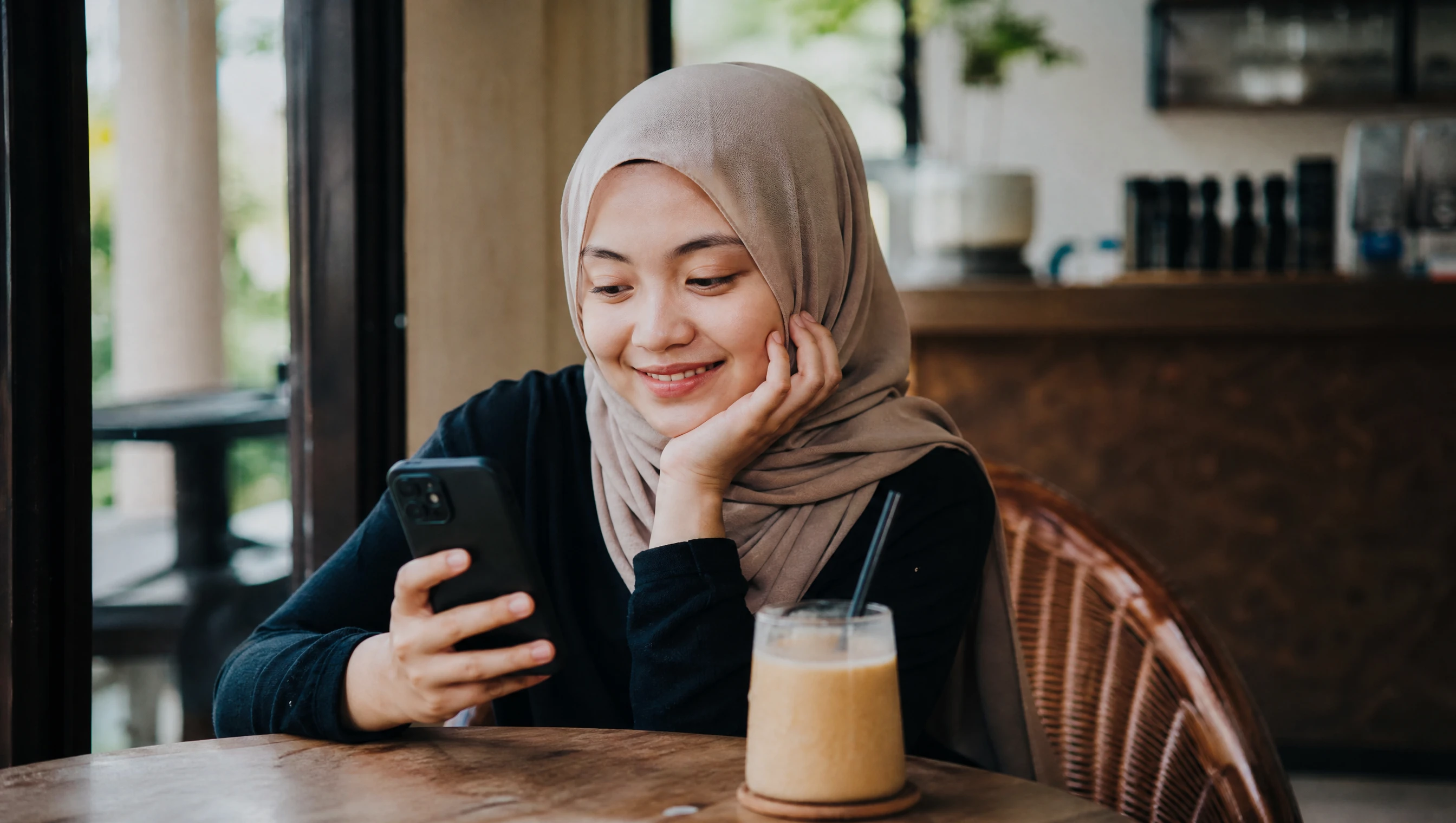 Pelanggan muda Malaysia sedang membeli-belah guna app shopping di telefon sambil duduk di kafe