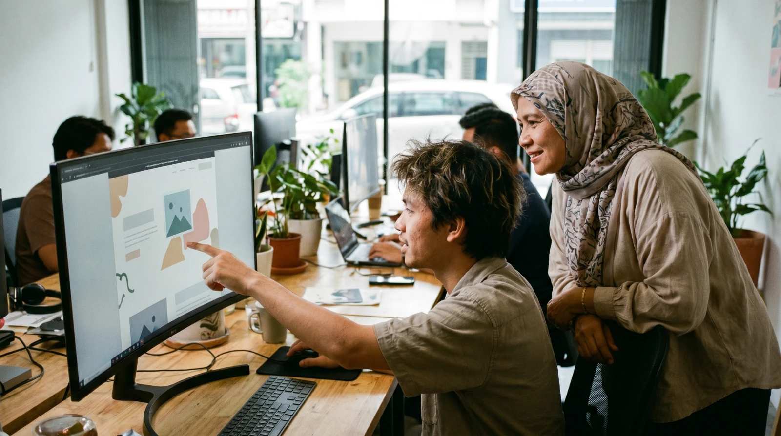 Pereka web Malaysia menunjukkan reka bentuk website kepada pemilik perniagaan kecil di studio kreatif