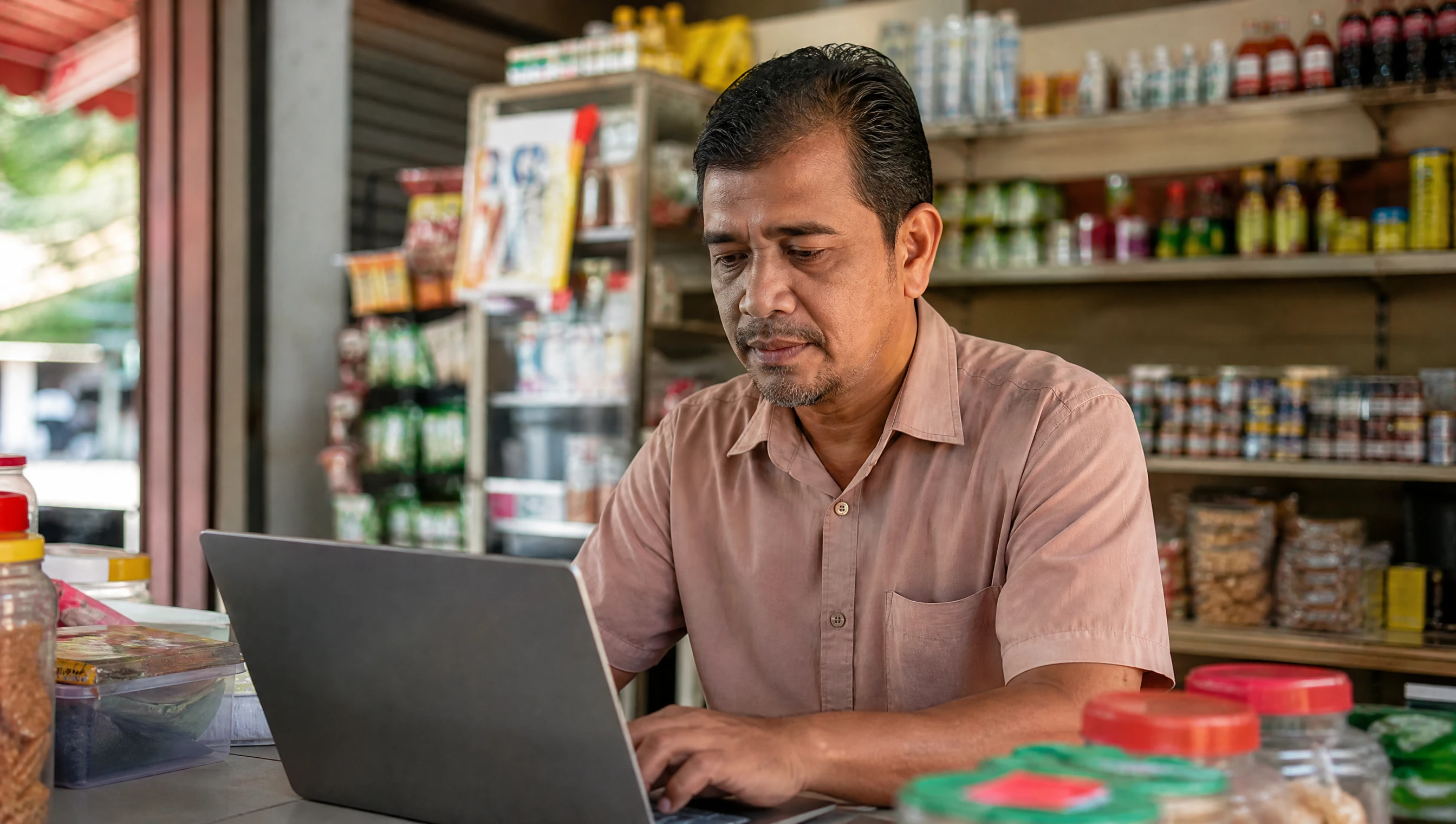 Pemilik kedai runcit Malaysia mengemaskini maklumat bisnes di komputer riba dalam kedai