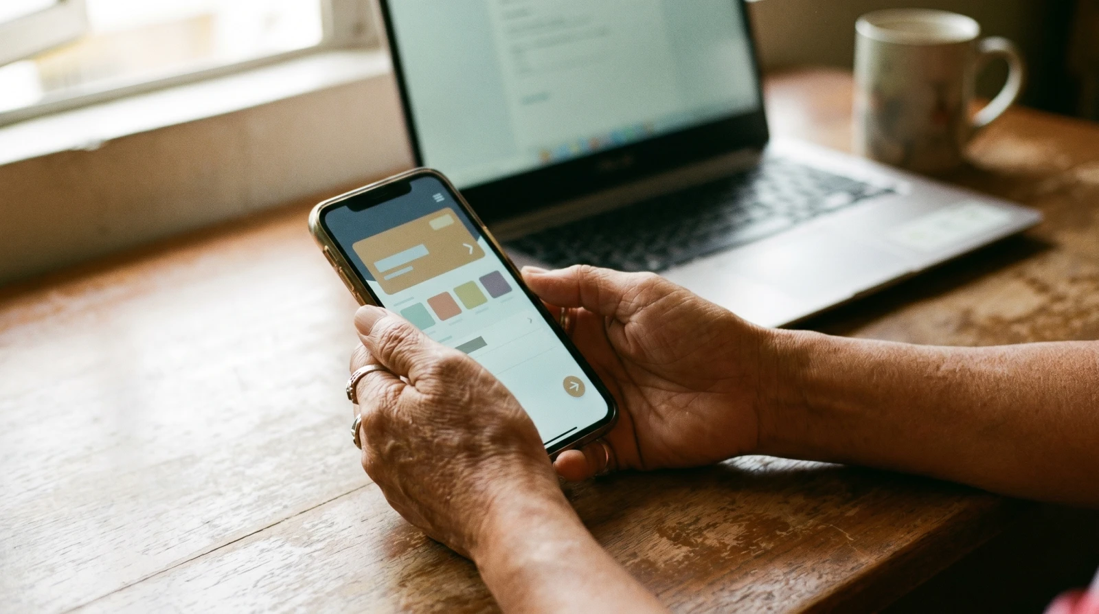 Tangan memegang telefon pintar menunjukkan skrin pemindahan online banking di meja kerja