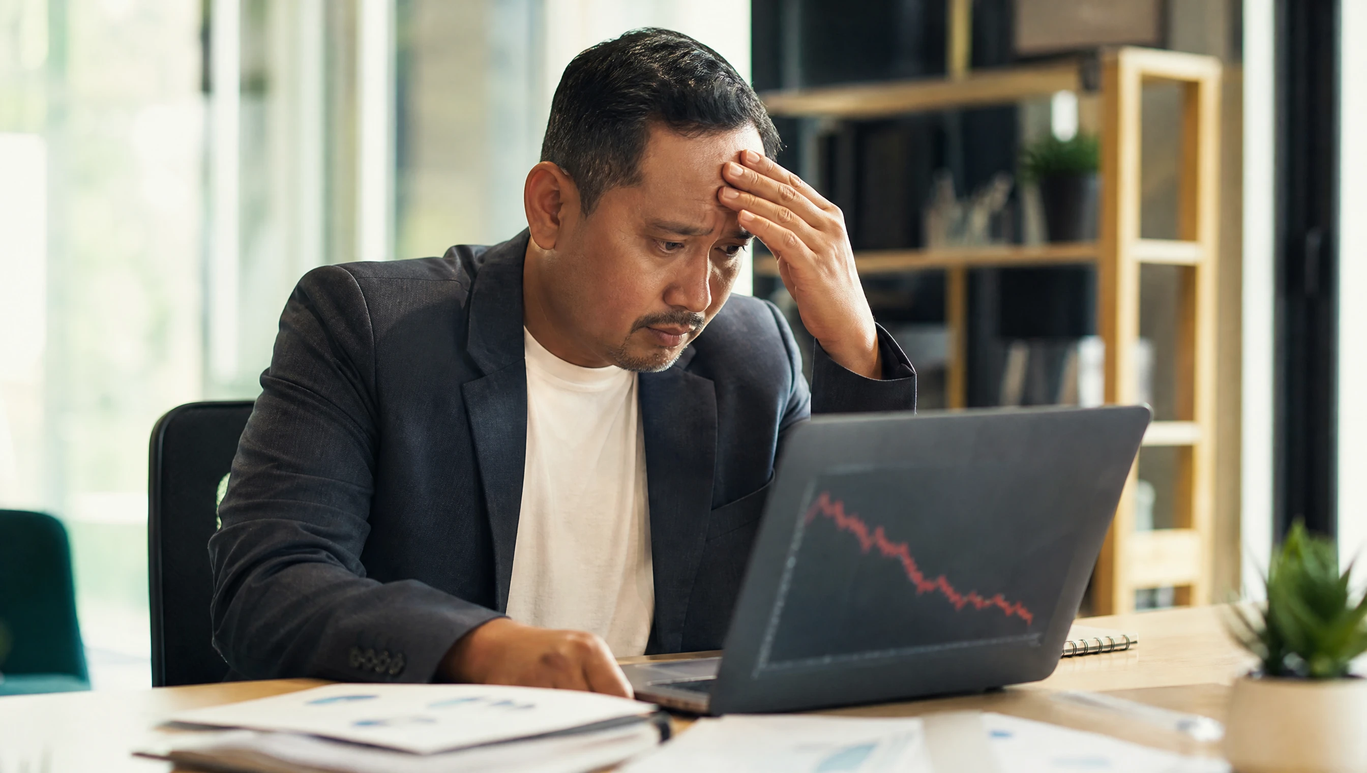 Pemilik bisnes Malaysia melihat graf ranking menurun pada skrin laptop dengan wajah risau di pejabat