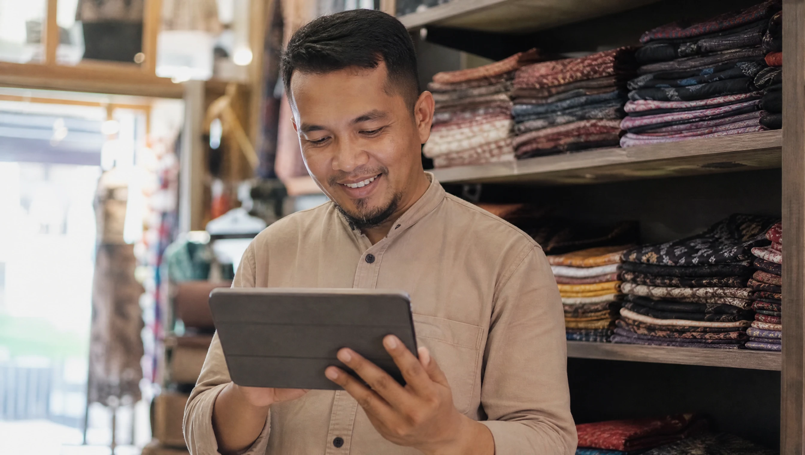 Pemilik bisnes Malaysia tersenyum melihat website barunya di tablet dalam kedai