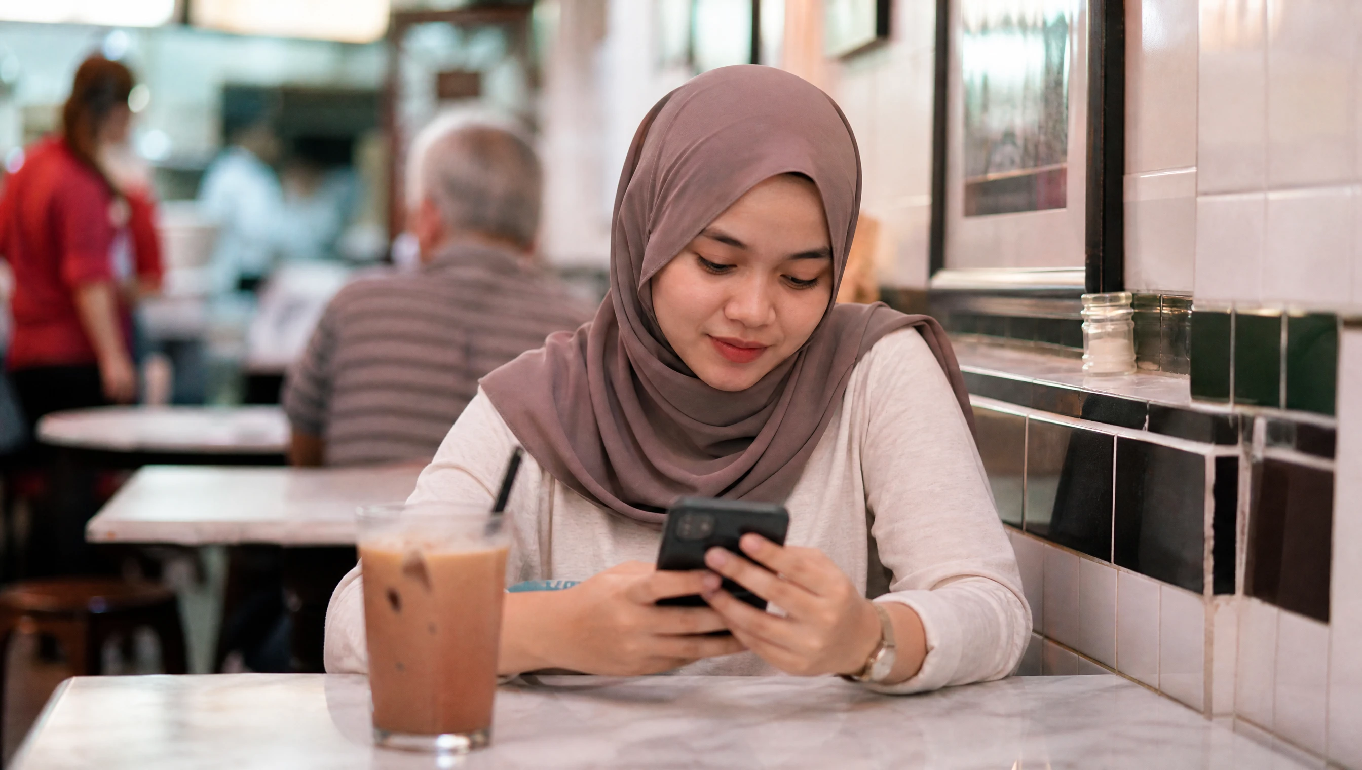 Young Malaysian woman checking a business website on her phone at a kopitiam