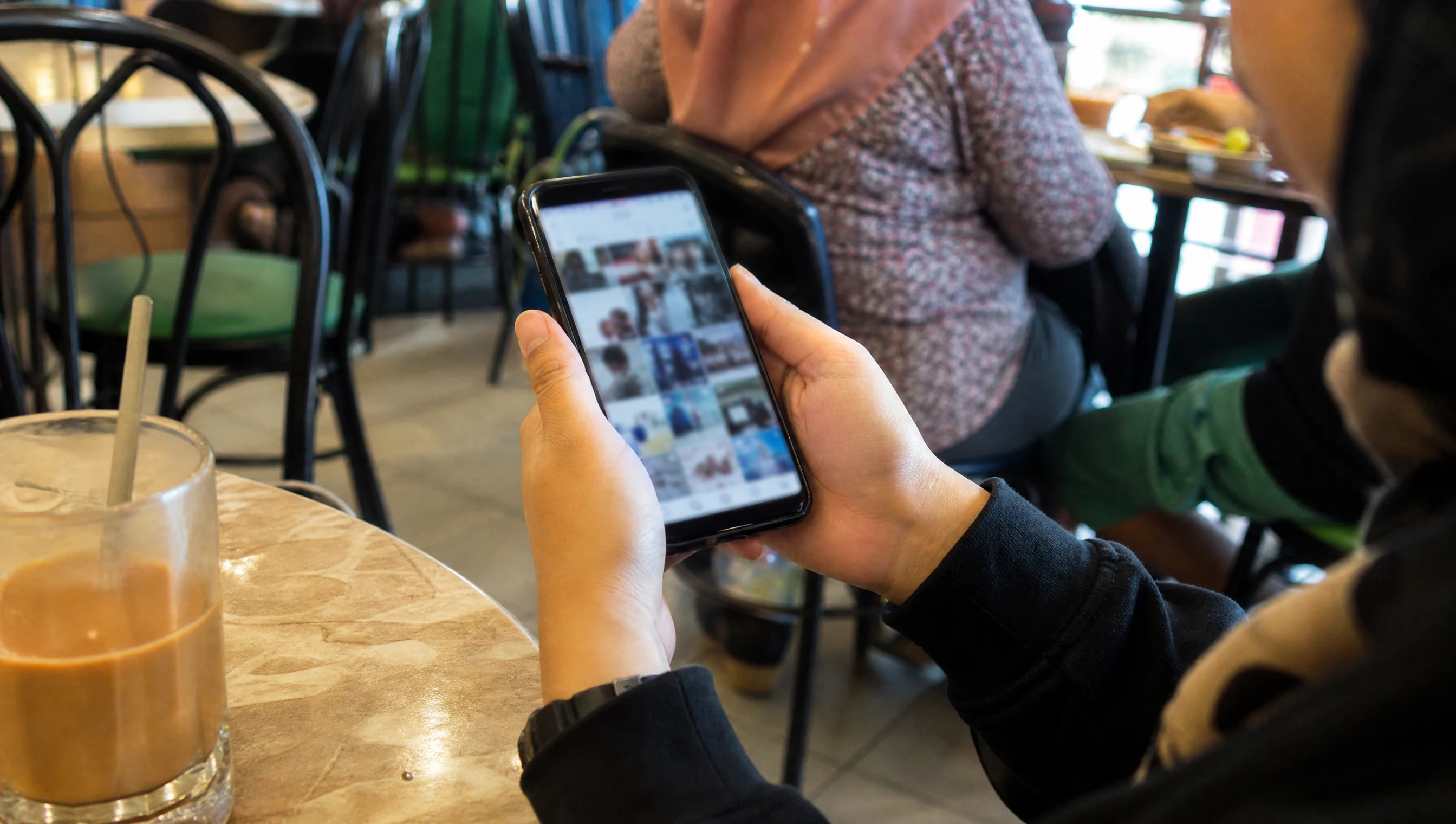 Hands scrolling a busy social media feed on a phone at a Malaysian cafe