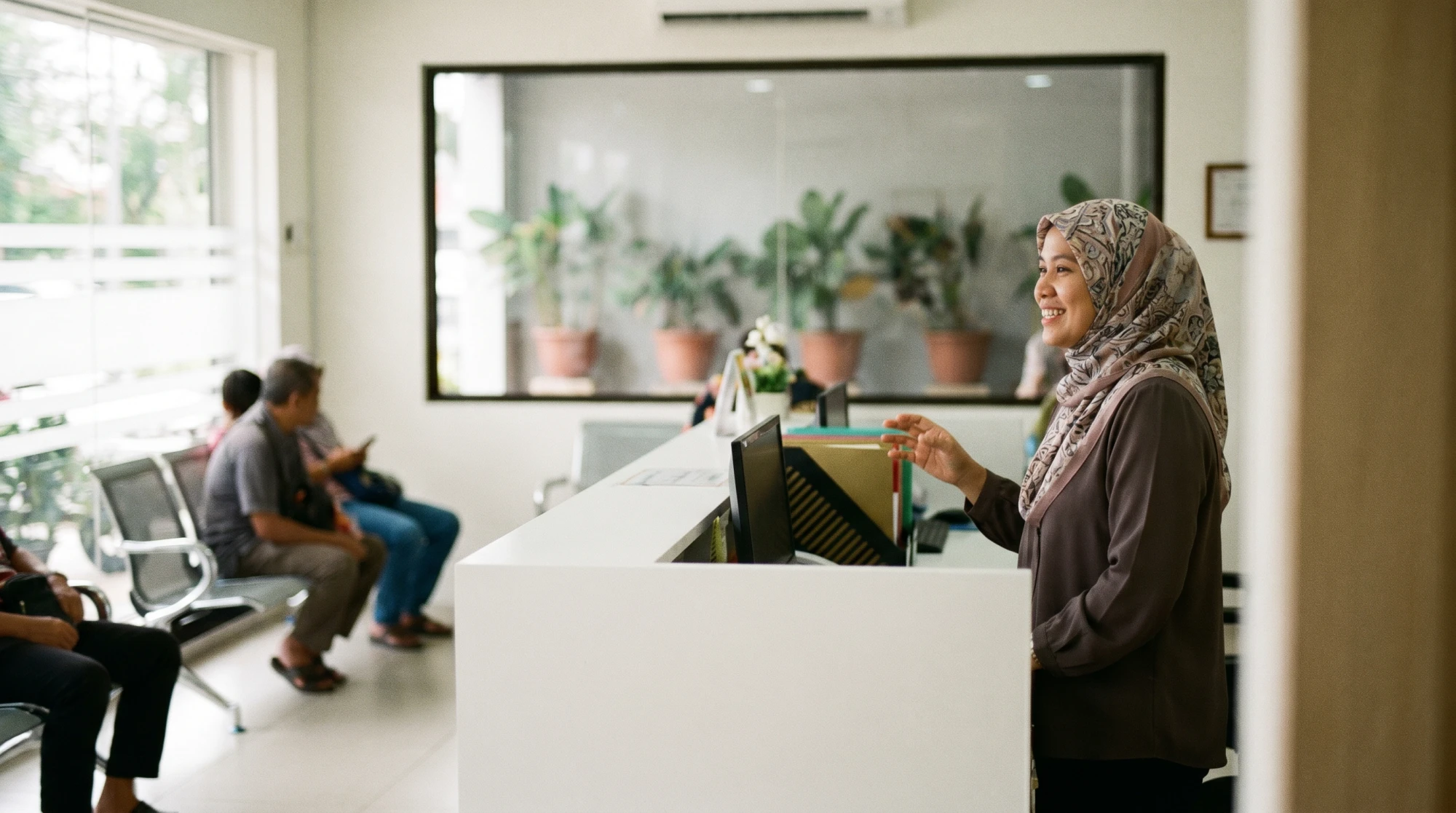 Kaunter penyambut tetamu klinik moden di Malaysia dengan staf wanita bertudung tersenyum
