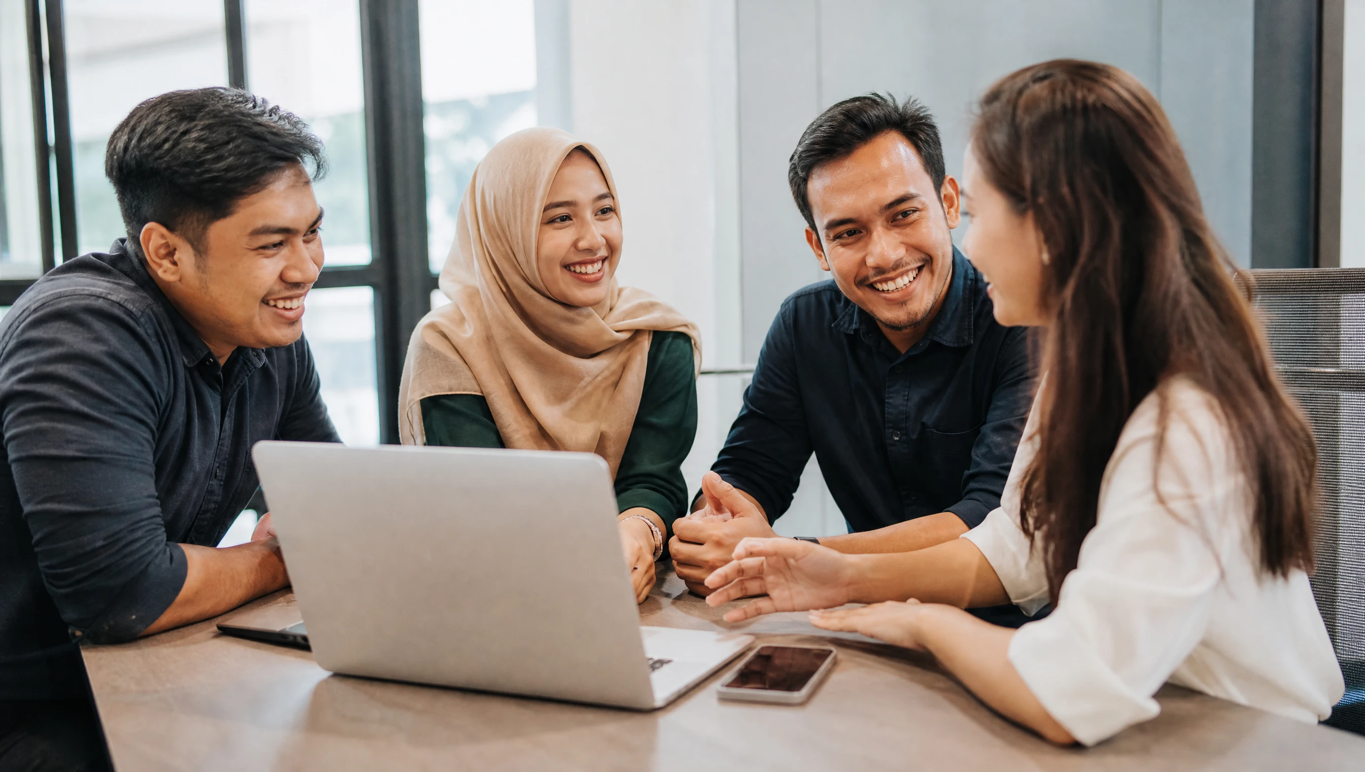 Malaysian app team discussing a project with a client over a phone and laptop
