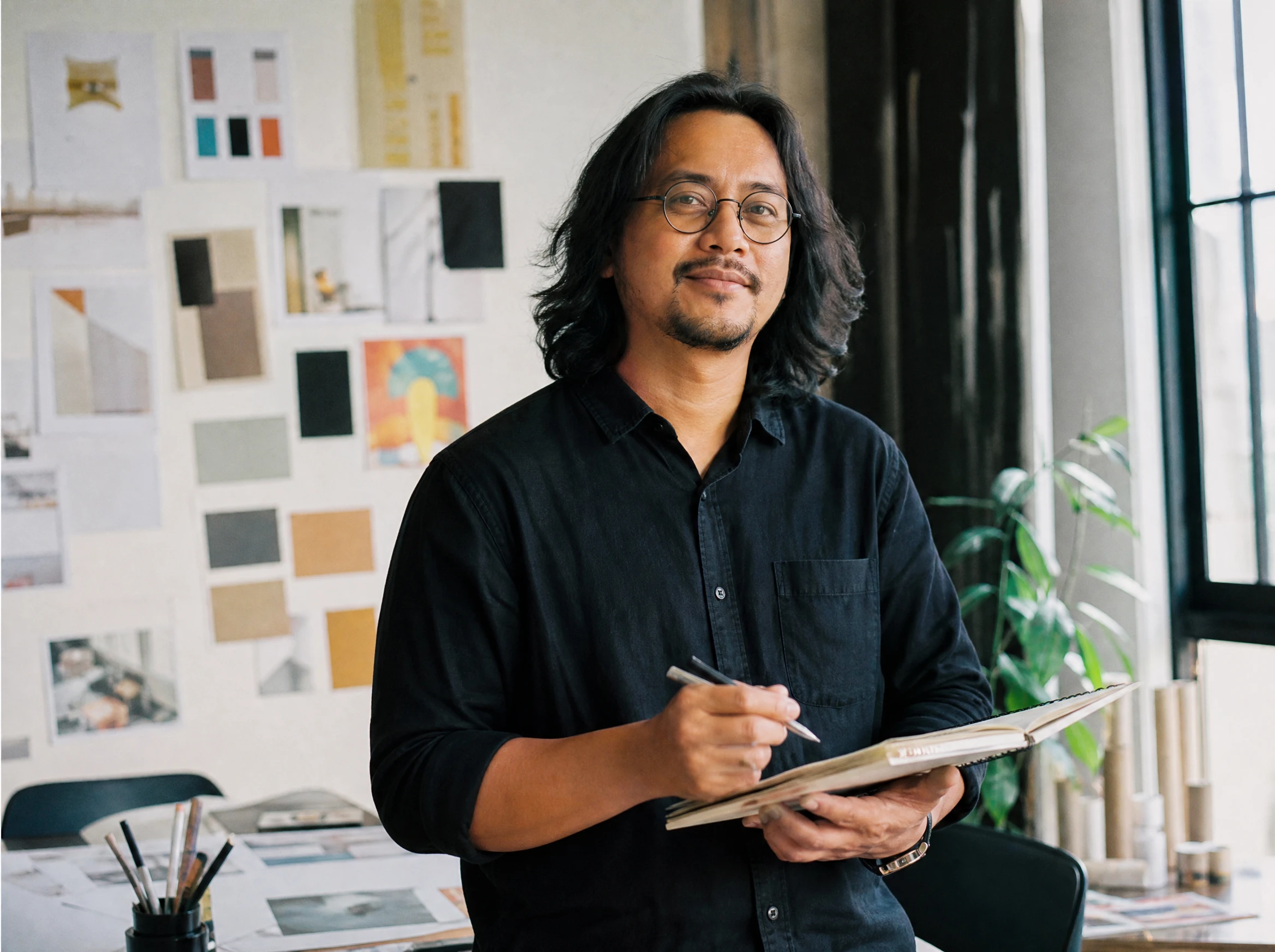 Confident Malaysian creative director in a design studio holding a sketchbook