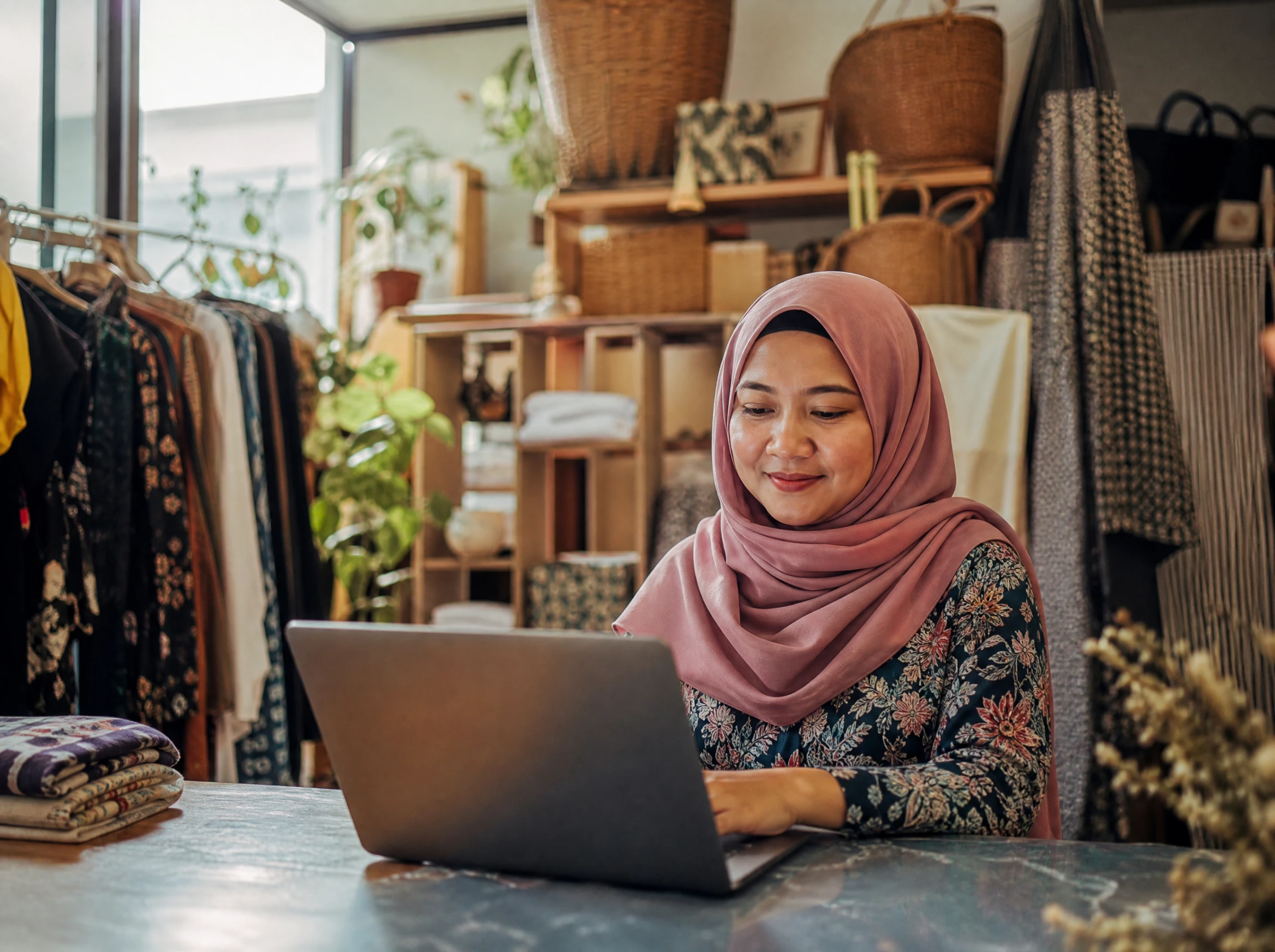 Relaxed Malaysian shop owner working calmly on her laptop, site running smoothly