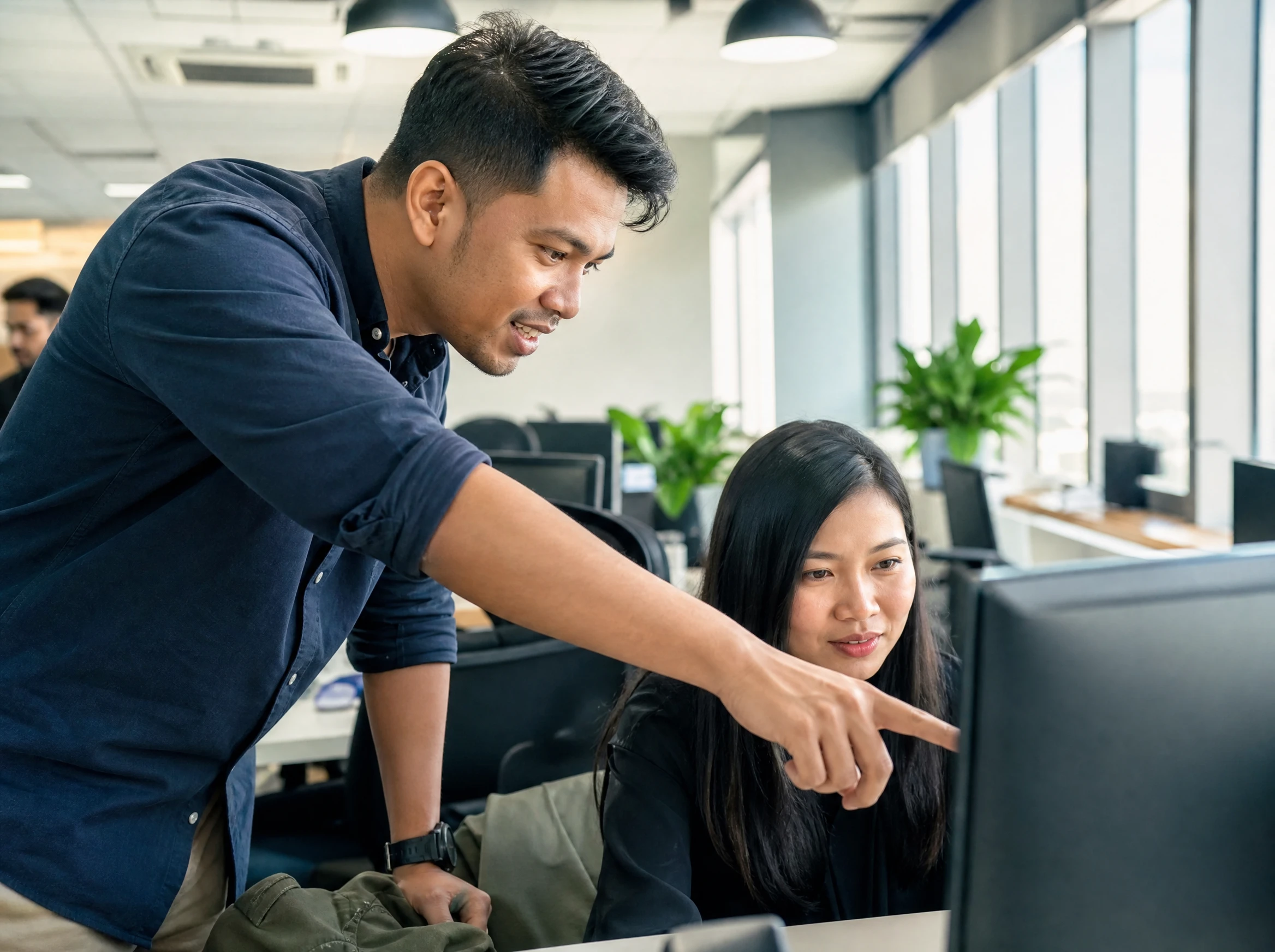 Malaysian support engineer helping an office staff member at her workstation