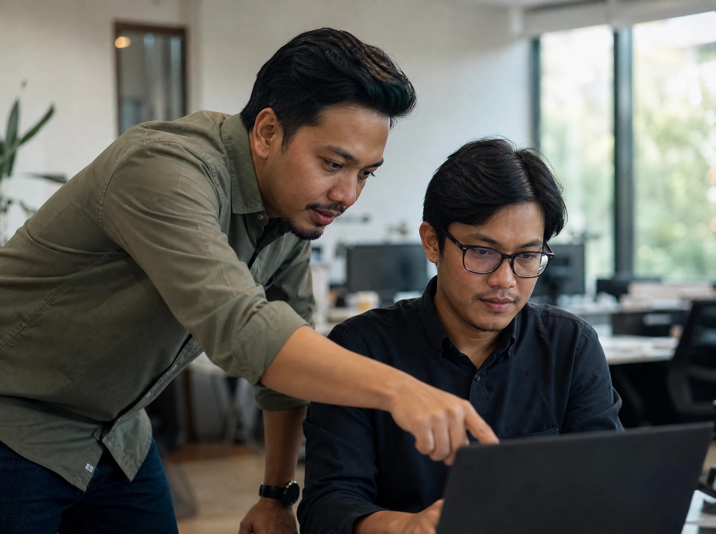 Malaysian developer helping a colleague at a laptop