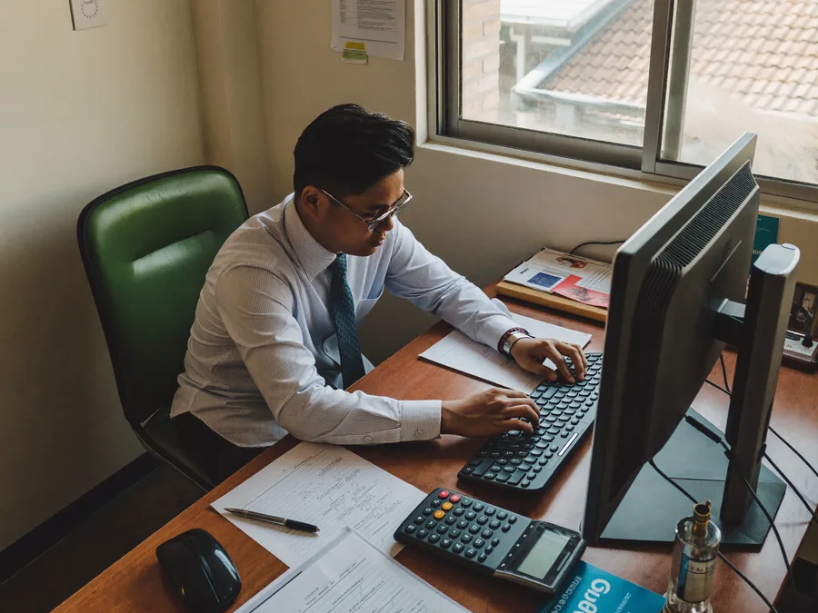 Malaysian accountant working at a desktop computer in a small office