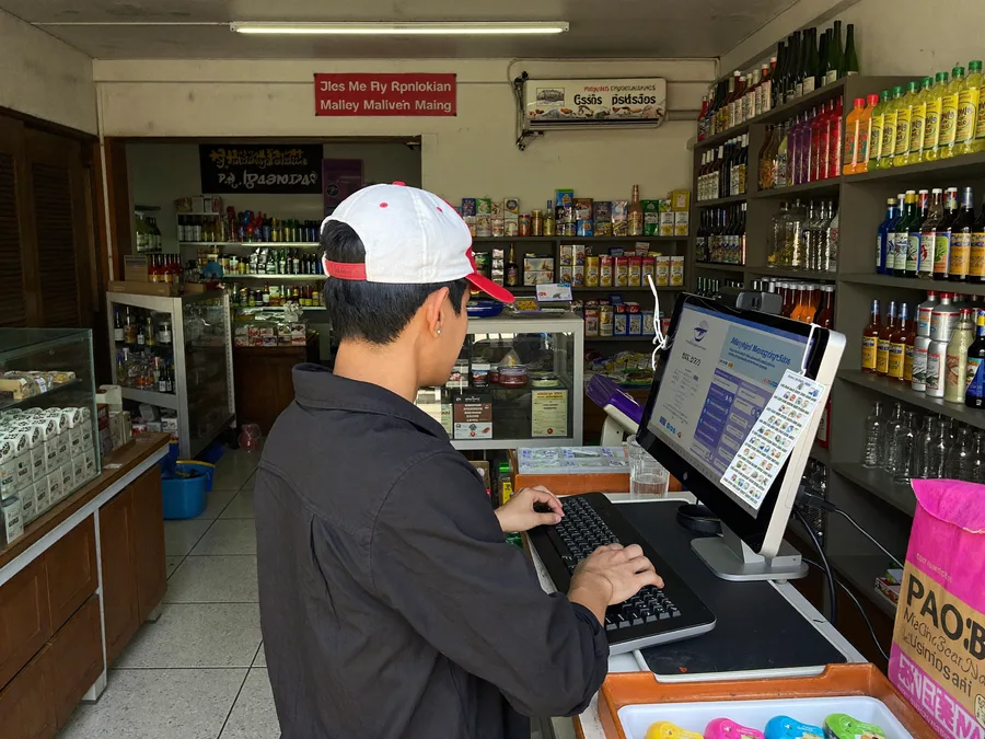 Malaysian shopkeeper using a desktop POS computer at a retail counter